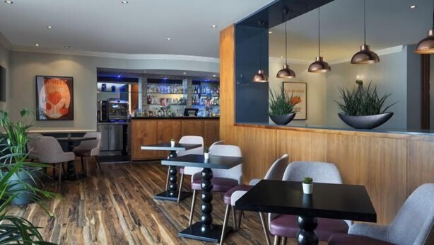 A modern bar area with wooden flooring, bar stools, and pendant lighting. - Delta Hotels by Marriott Peterborough (Orton Waterville)