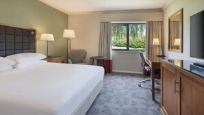 A hotel room with a large bed, two bedside lamps, a desk with a chair, a television, and a window with curtains. - Delta Hotels by Marriott Peterborough (Orton Waterville)