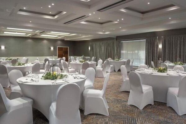 A conference room with round tables, white chairs, and a carpeted floor.