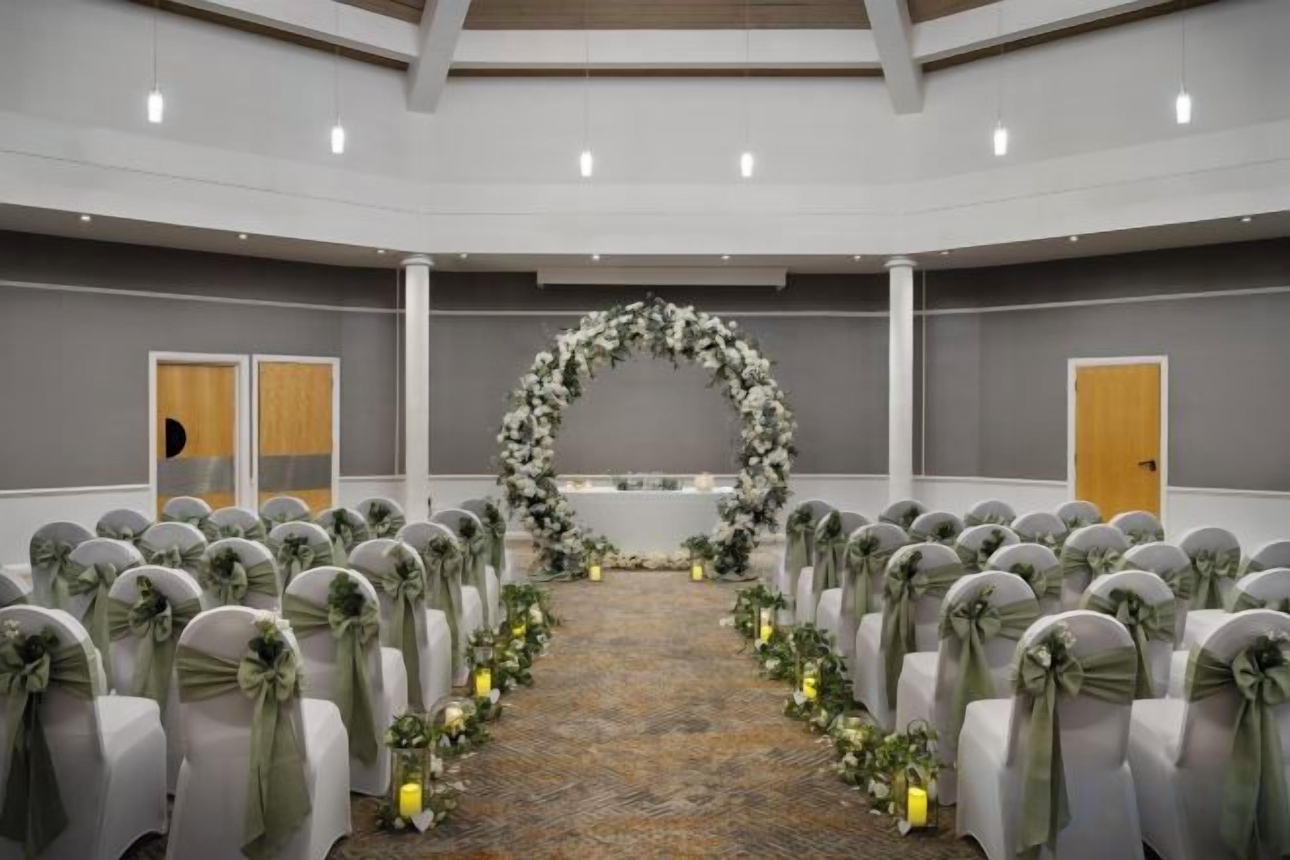 Een vergaderzaal met rijen stoelen, een bloemrijke boog en een tapijtvloer.