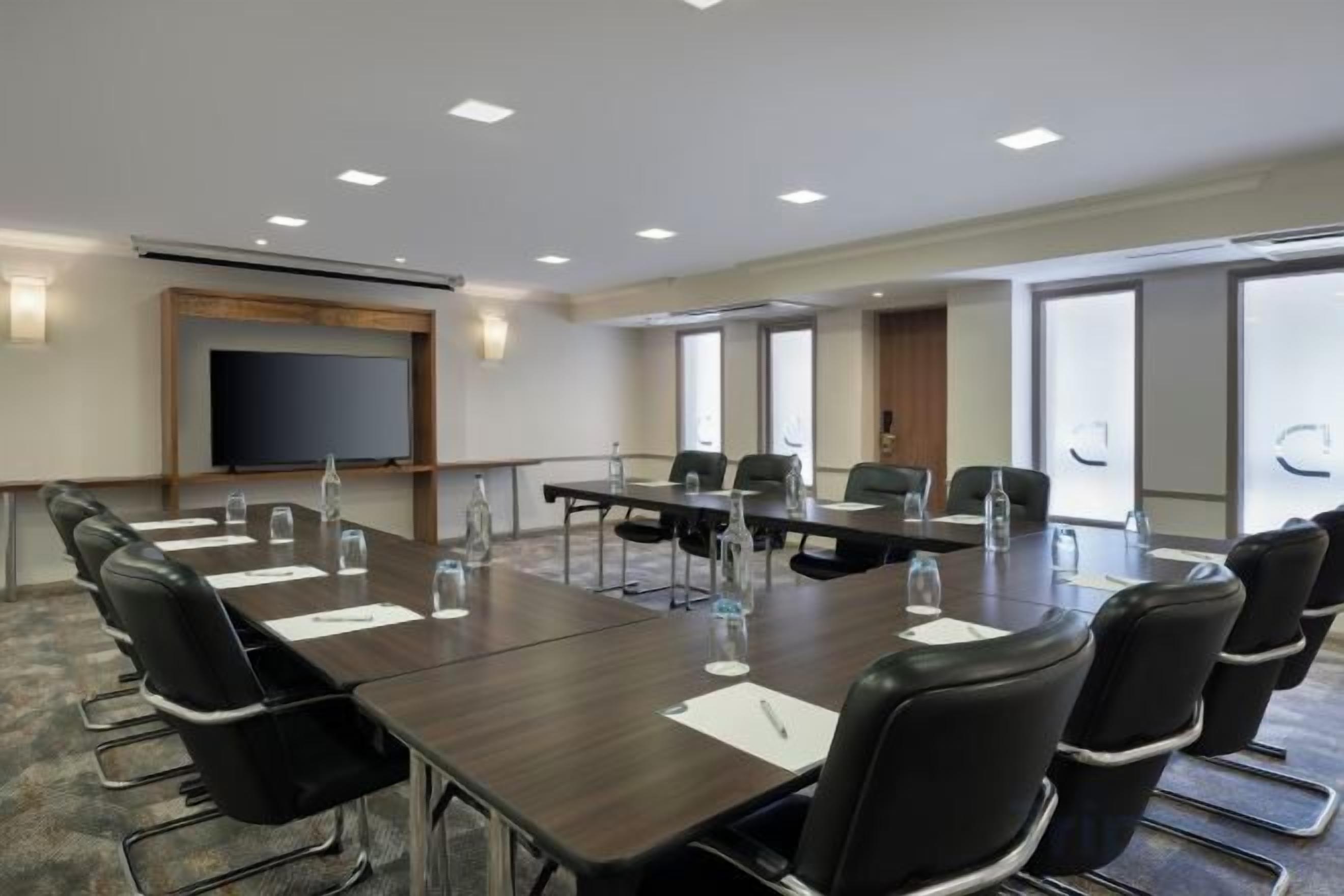 A conference room with a long table, chairs, a projector screen, and a large window.