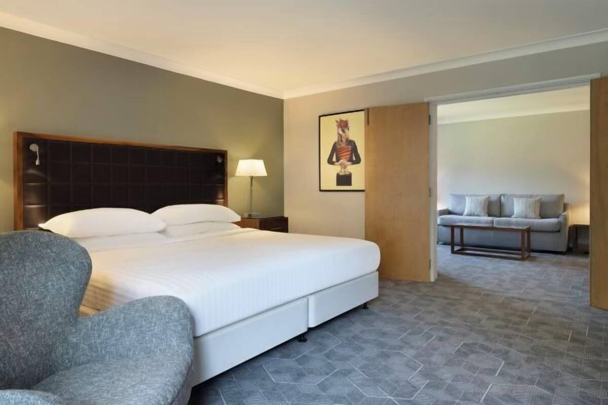 A hotel room with a bed, a chair, a sofa, a lamp, and a painting on the wall.