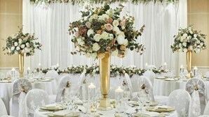 A banquet hall with round tables set for a formal event, featuring floral centerpieces and white tablecloths. - Delta Hotels by Marriott Peterborough (Orton Waterville)