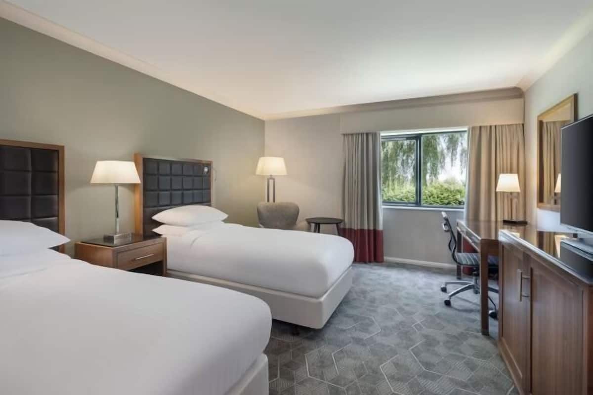 A hotel room with two beds, a desk, a chair, a TV, and a window with curtains.