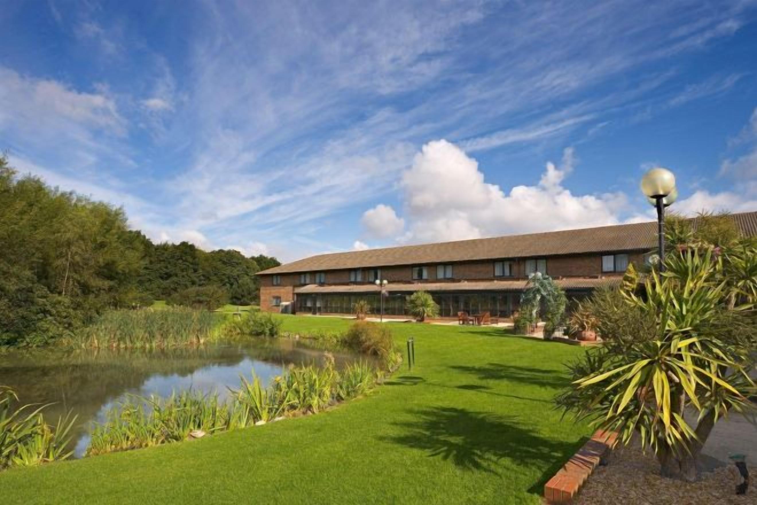A hotel with a large building, a pond, and well-maintained lawn.