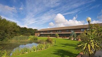 A hotel with a large building, a pond, and well-maintained lawn.