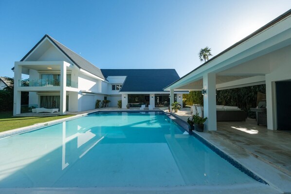 Ein modernes, zweistöckiges Haus mit großem Swimmingpool, überdachten Sitzbereichen und einem gepflegten Garten.