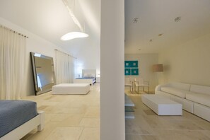 Ein modernes Hotelzimmer mit einem großen Bett, einer Sitzecke mit Sofa und Sesseln, einem Flachbildfernseher und einem großen Fenster mit Vorhängen.