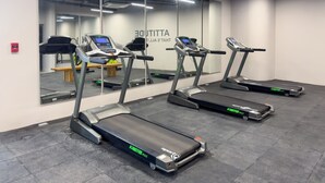 Une salle de sport équipée de tapis de course, d’un mur recouvert de miroirs et d’un banc en bois.