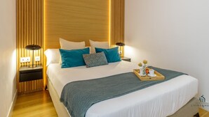 Une chambre d’hôtel moderne avec un grand lit, deux tables de chevet avec des lampes, une tête de lit en bois et un plateau contenant des articles pour le petit-déjeuner.
