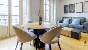 Un salon moderne avec une table ronde en bois, deux fauteuils gris à revêtement en tissu, un canapé gris avec des coussins bleus et une table basse noire.