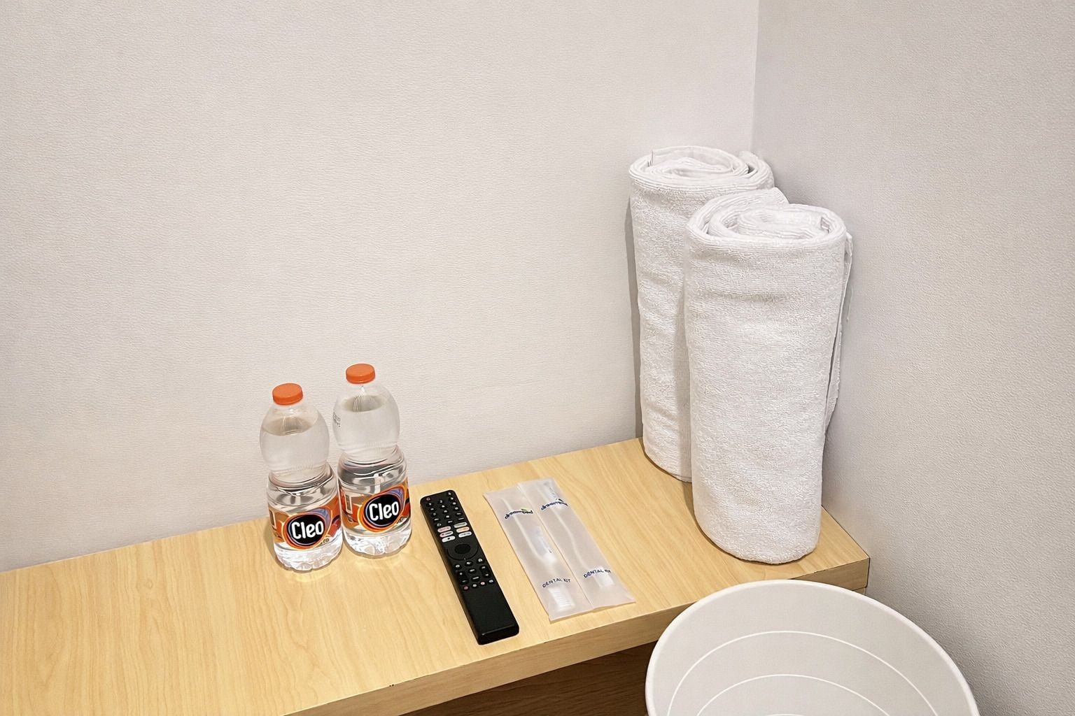 A wooden table with toiletries including two bottles of water, a remote control, and a towel.