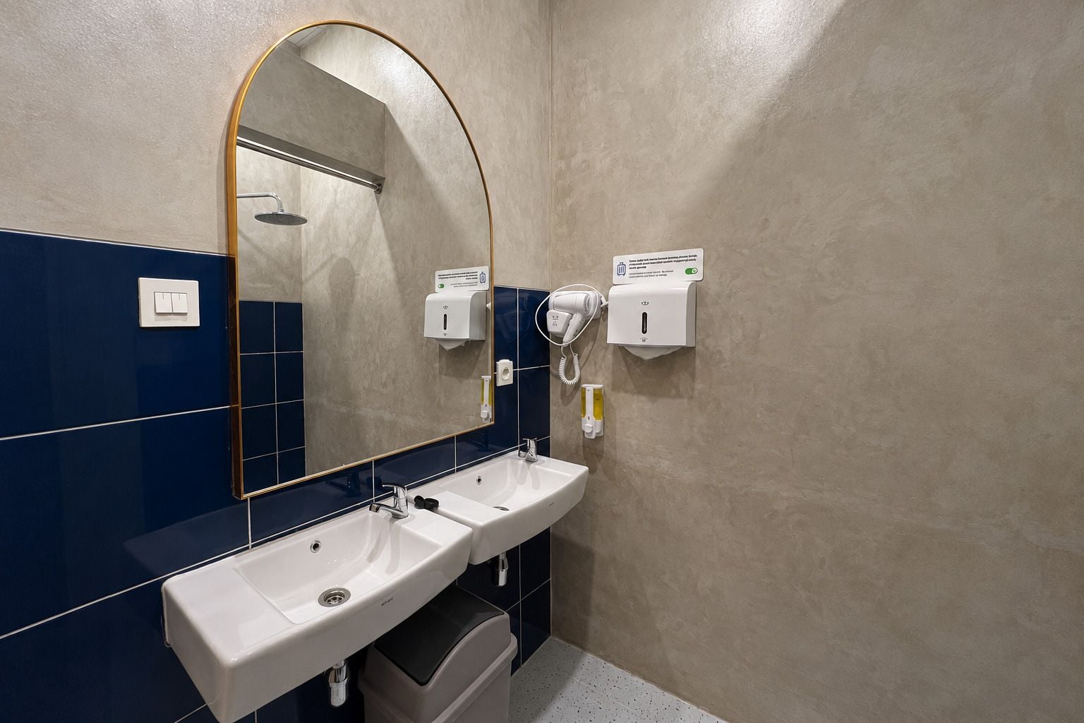 A bathroom with a large mirror, two sinks, a towel dispenser, and a hand dryer.