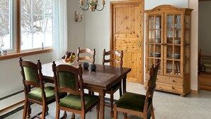 A dining room with a wooden table, green upholstered chairs, a fruit bowl, and a wooden cabinet with glass doors. - 3 bedroom cozy apartment in Verma (Verma)