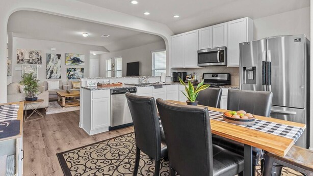 A modern kitchen with white cabinetry, stainless steel appliances, and a dining area with a checkered tablecloth. - Convenient Family Home in Heart of Conroe (Conroe)