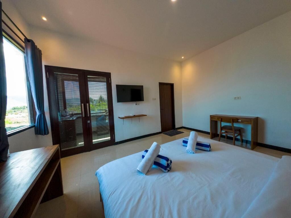 Een moderne hotelkamer met een groot bed, een bureau, een televisie en een schuifdeur naar buiten.