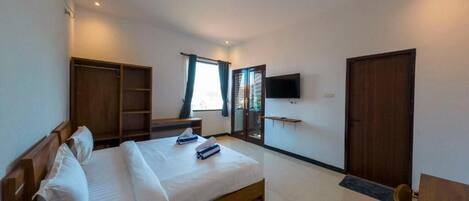 A bedroom with a bed, a TV mounted on the wall, a wardrobe, and a desk.