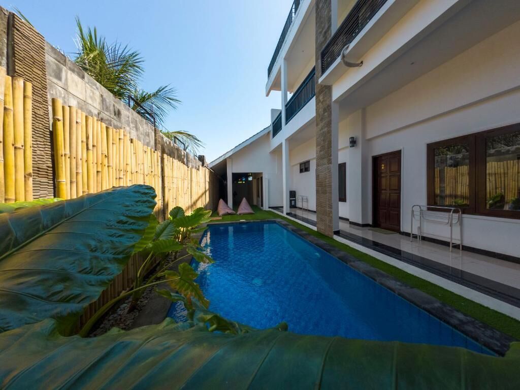 A swimming pool with a bamboo fence on one side, a covered area with a bench, and a building with a balcony and windows.