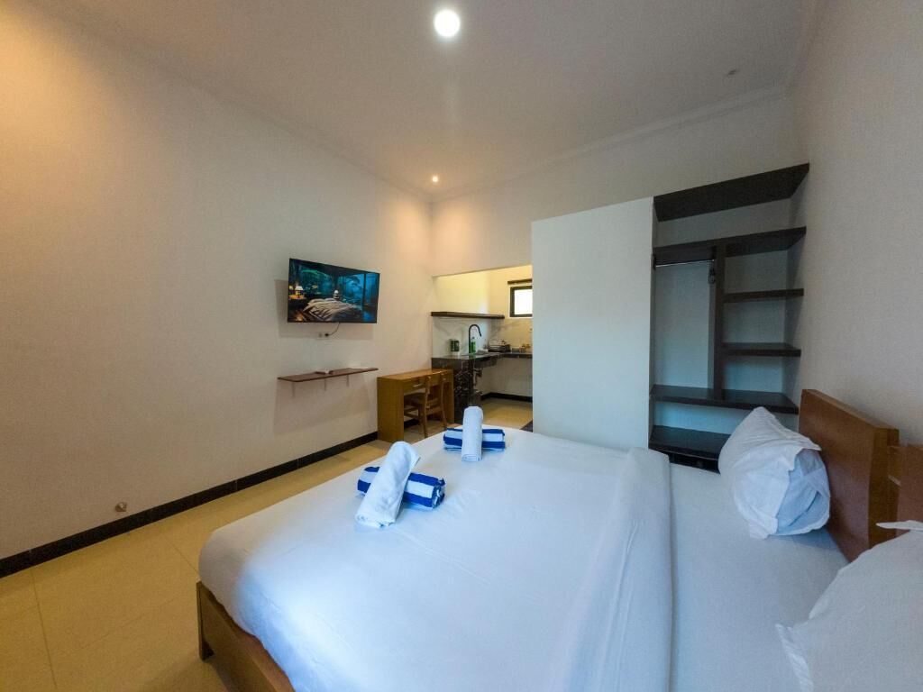 A hotel room with a bed, a television, a desk, and a view of the kitchen.