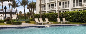 A swimming pool with lounge chairs, palm trees, and a building with balconies. - Wyndham Sea Gardens 2 BR Condo - Beach Access! (Pompano Beach)