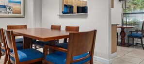 A dining area with a wooden table and blue cushioned chairs, a kitchen area with wooden cabinets, and a window with blinds. - Wyndham Sea Gardens 2 BR Condo - Beach Access! (Pompano Beach)