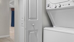 Un lavadero con lavadora y secadora, una puerta que da a otra habitación y una lámpara fijada a la pared.