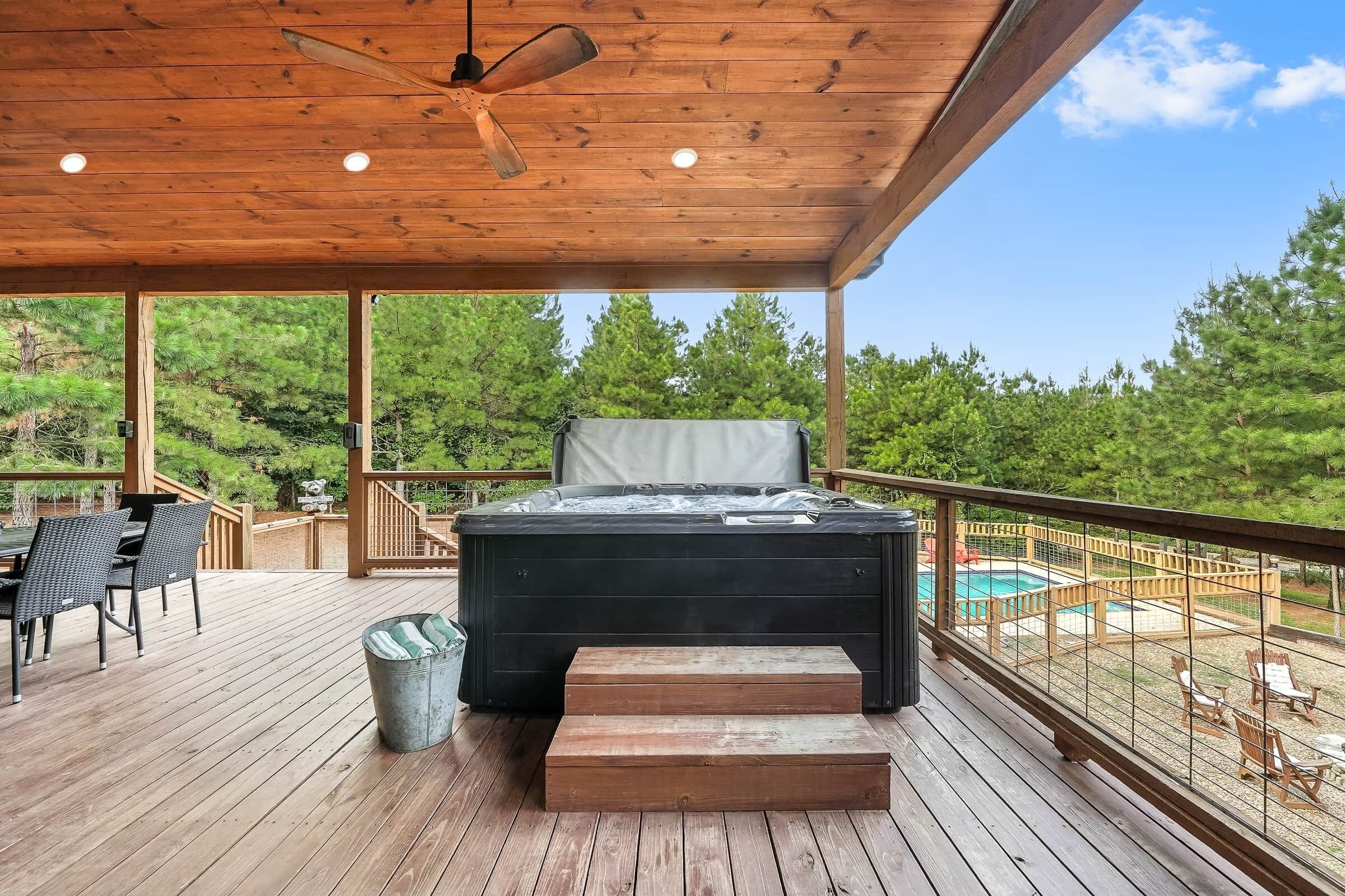 A wooden deck with a hot tub, outdoor seating, and a view of trees.