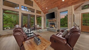 A spacious living room with leather sofas, a fireplace, large windows, and a TV. - Hochatown Cabin Private Pool Hot Tub Game Room (Hochatown)