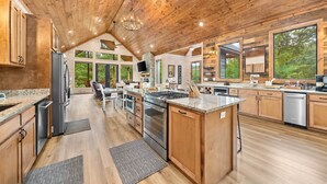 A spacious kitchen with wooden cabinets, granite countertops, stainless steel appliances, and large windows offering views of the outdoors. - Hochatown Cabin Private Pool Hot Tub Game Room (Hochatown)
