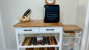 A white desk with drawers, a black microwave, a wooden shelf, a ceramic pig, a clock, and a metal cart. - Getaway beach house, Downstairs unit (Fort Myers Beach)