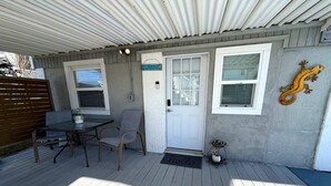 A covered patio with a table and chairs, a white door, and a decorative lizard on the wall. - Getaway beach house, Downstairs unit (Fort Myers Beach)