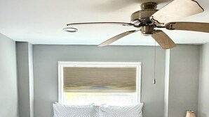 A bedroom with a bed, a ceiling fan, a window with blinds, and a bedside table with a lamp. - Getaway beach house, Downstairs unit (Fort Myers Beach)