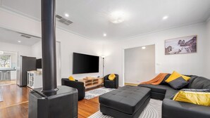 A modern living room with a fireplace, a flat-screen TV, a sofa, and a dining area visible in the background. - Spacious Multifunctional 5BR Retreat with Backyard (Bayswater)