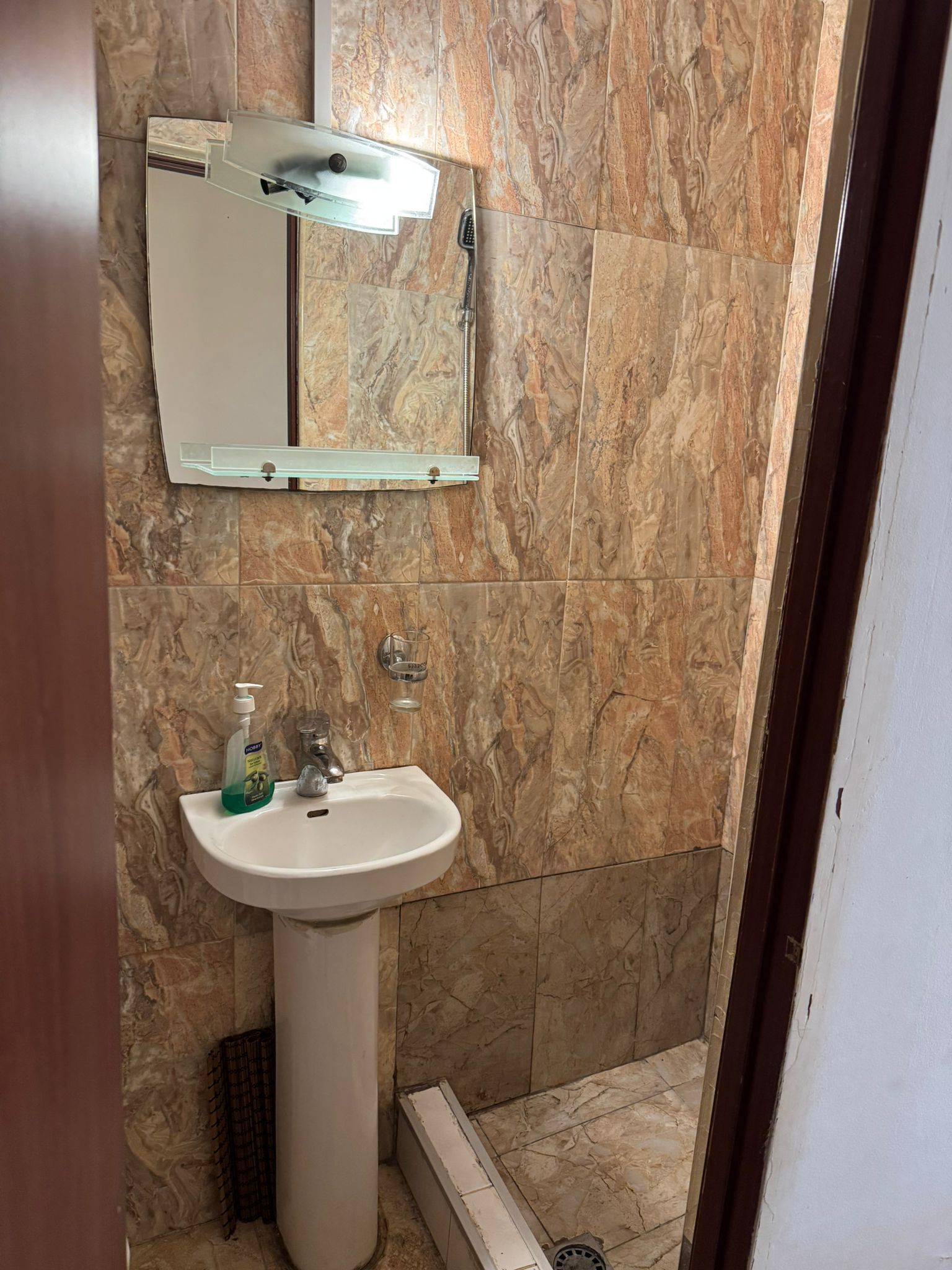 Een badkamer met een marmeren wand, een wastafel met zeepdispenser en een spiegel.