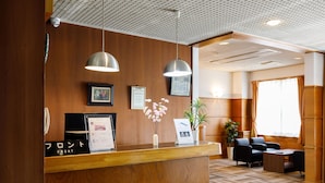 A reception area with a wooden reception desk, two pendant lights, framed certificates, a vase with flowers, and a seating area with a sofa and chairs.