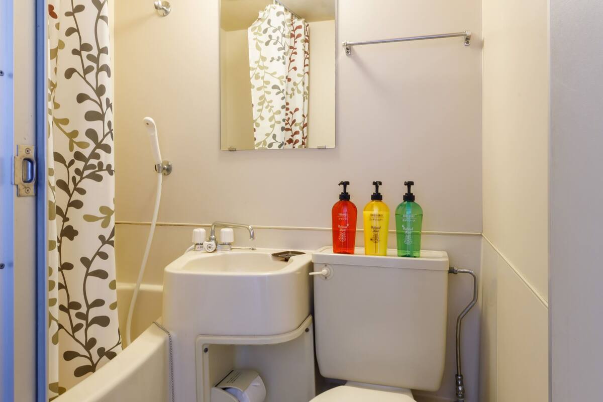 A small bathroom with a toilet, sink, and shower. There are three bottles of soap on the wall.