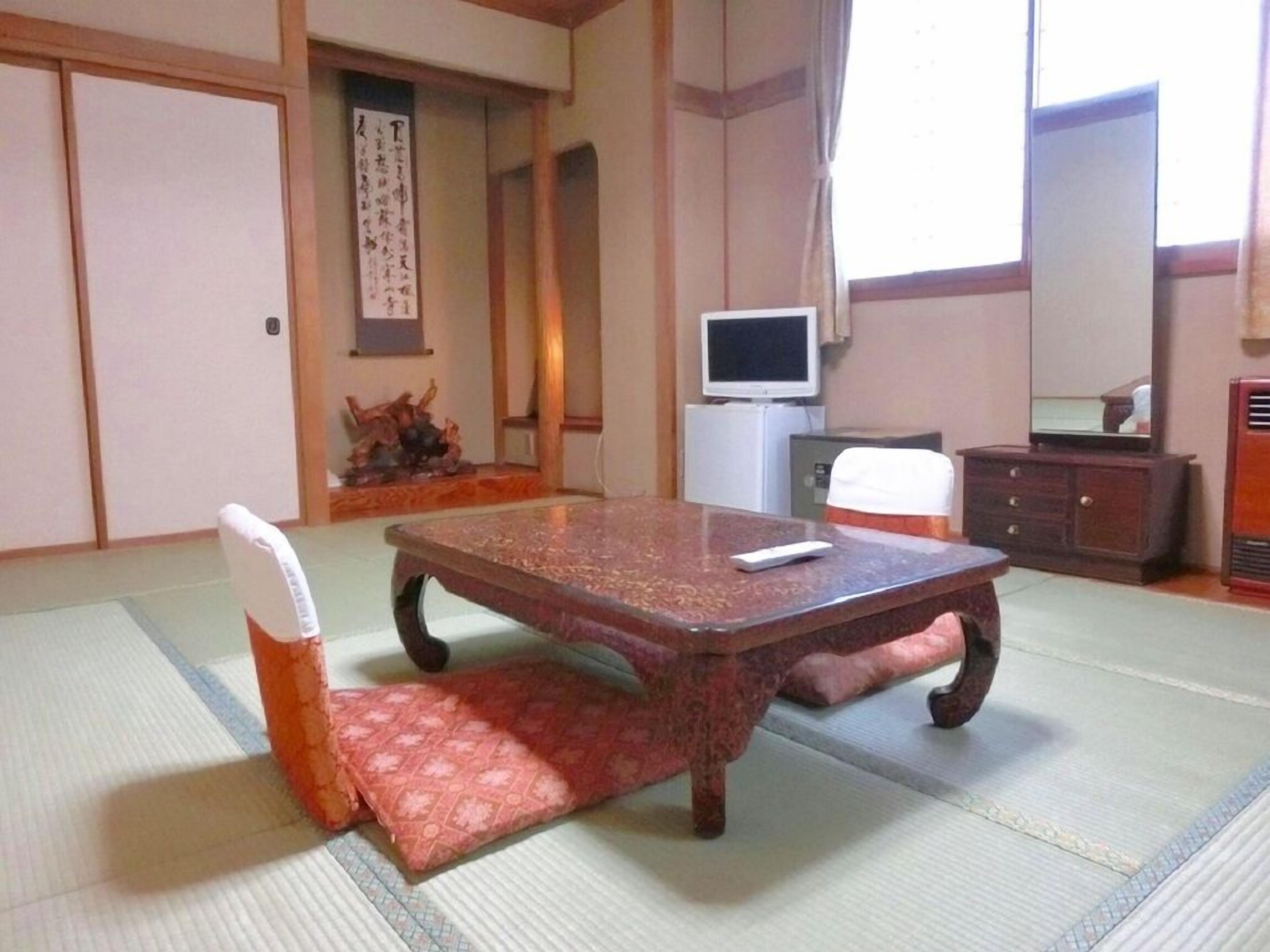 A traditional Japanese room with tatami flooring, a low table, a television, and a cabinet.