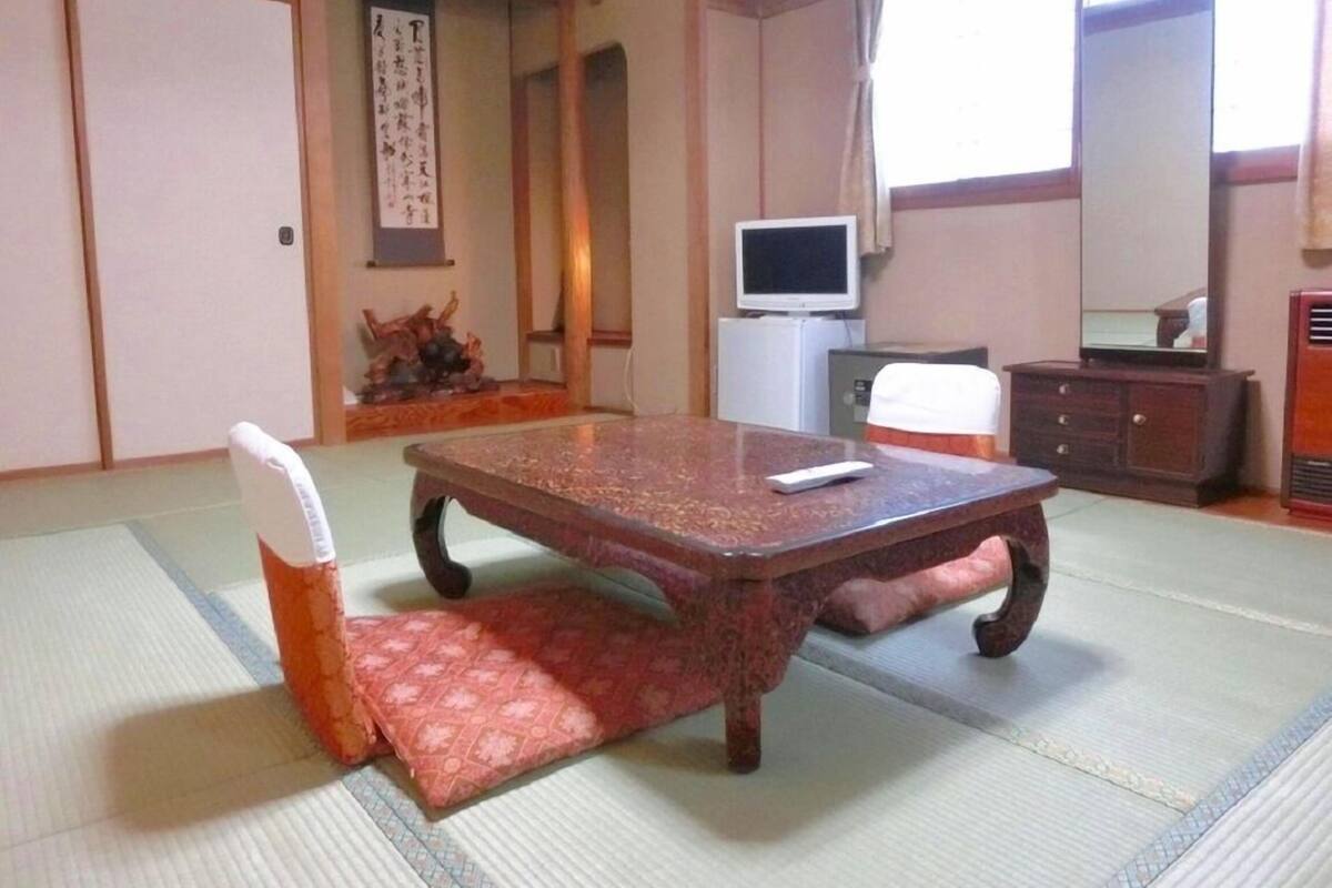 A traditional Japanese room with tatami flooring, a low table, a television, and a cabinet.