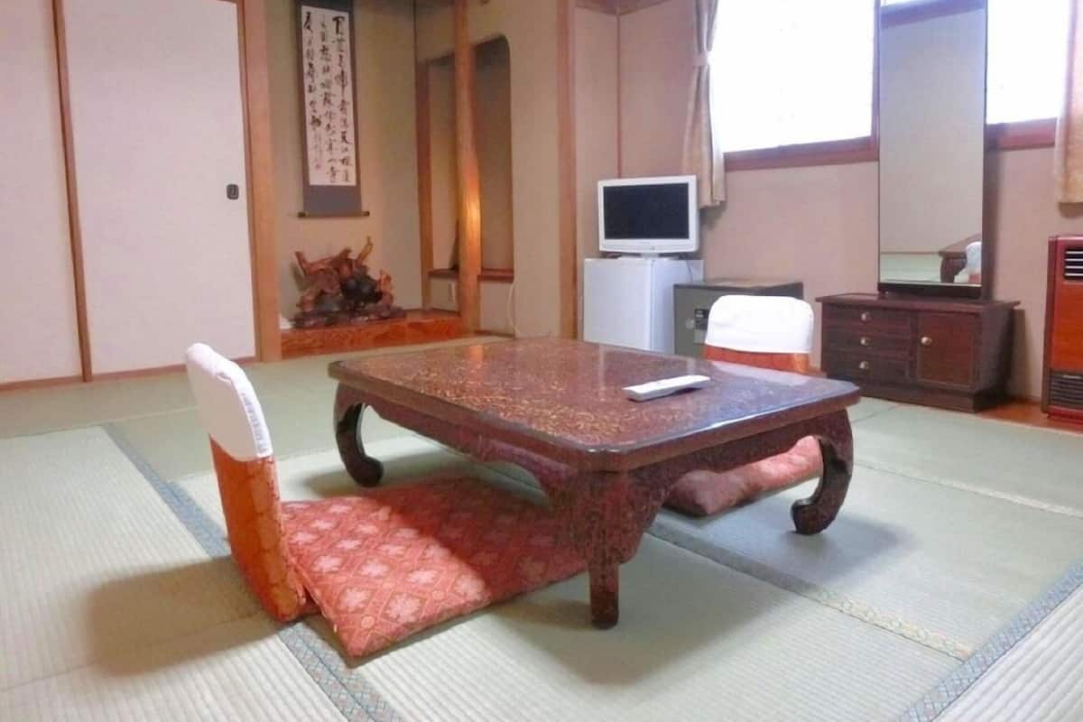 A traditional Japanese room with tatami flooring, a low table, a television, and a cabinet.