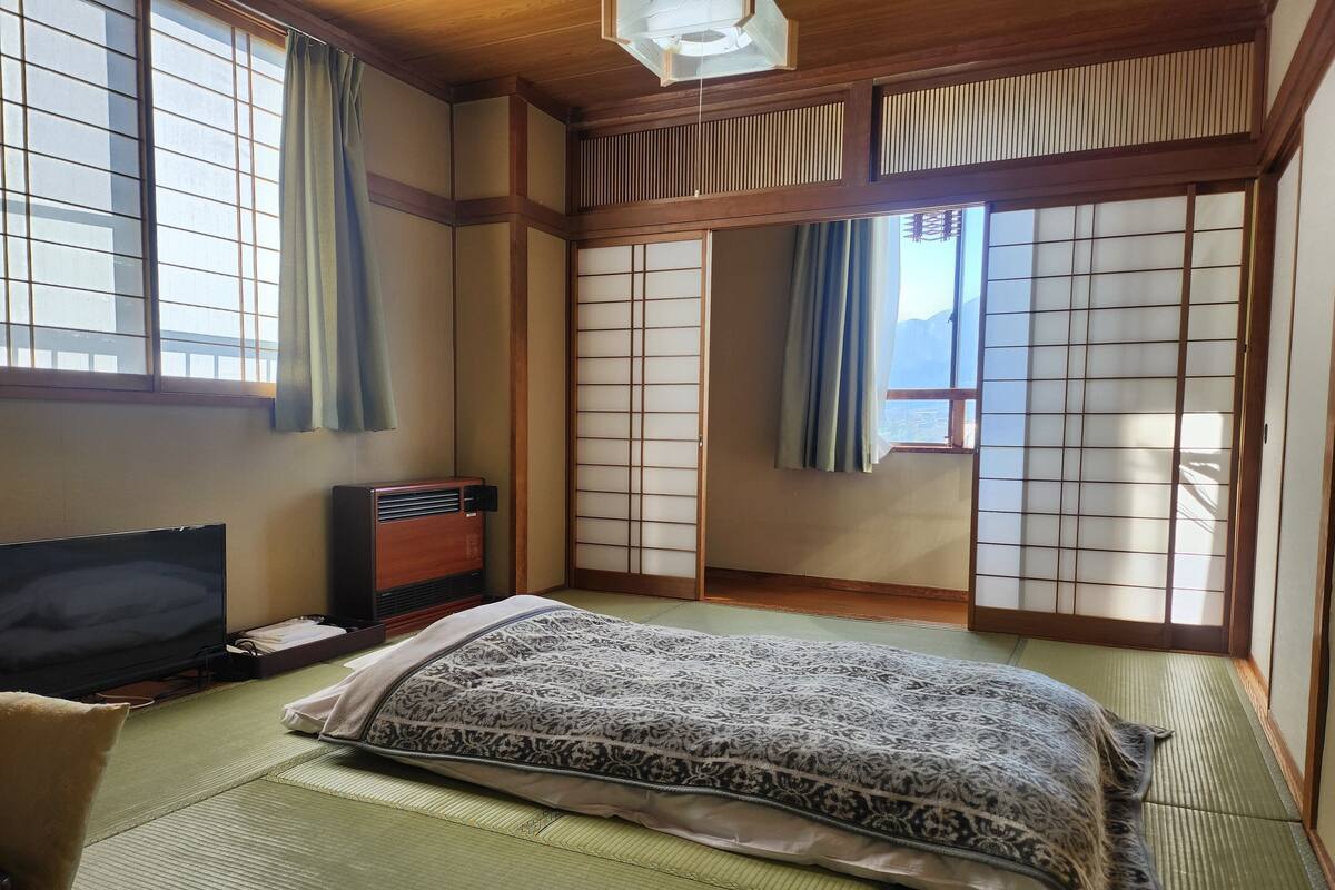A traditional Japanese-style room with tatami flooring, a bed with patterned bedding, a television, and sliding shoji doors.