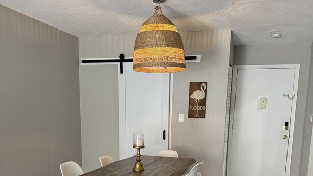 Een eethoek met een houten tafel en witte stoelen, een hanglamp en een deur met een 'FLORIDA' bord.