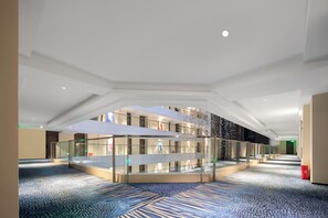 Un hall d’hôtel spacieux, doté d’une vitrine centrale en verre, d’un tapis à motifs et d’un plafond haut.