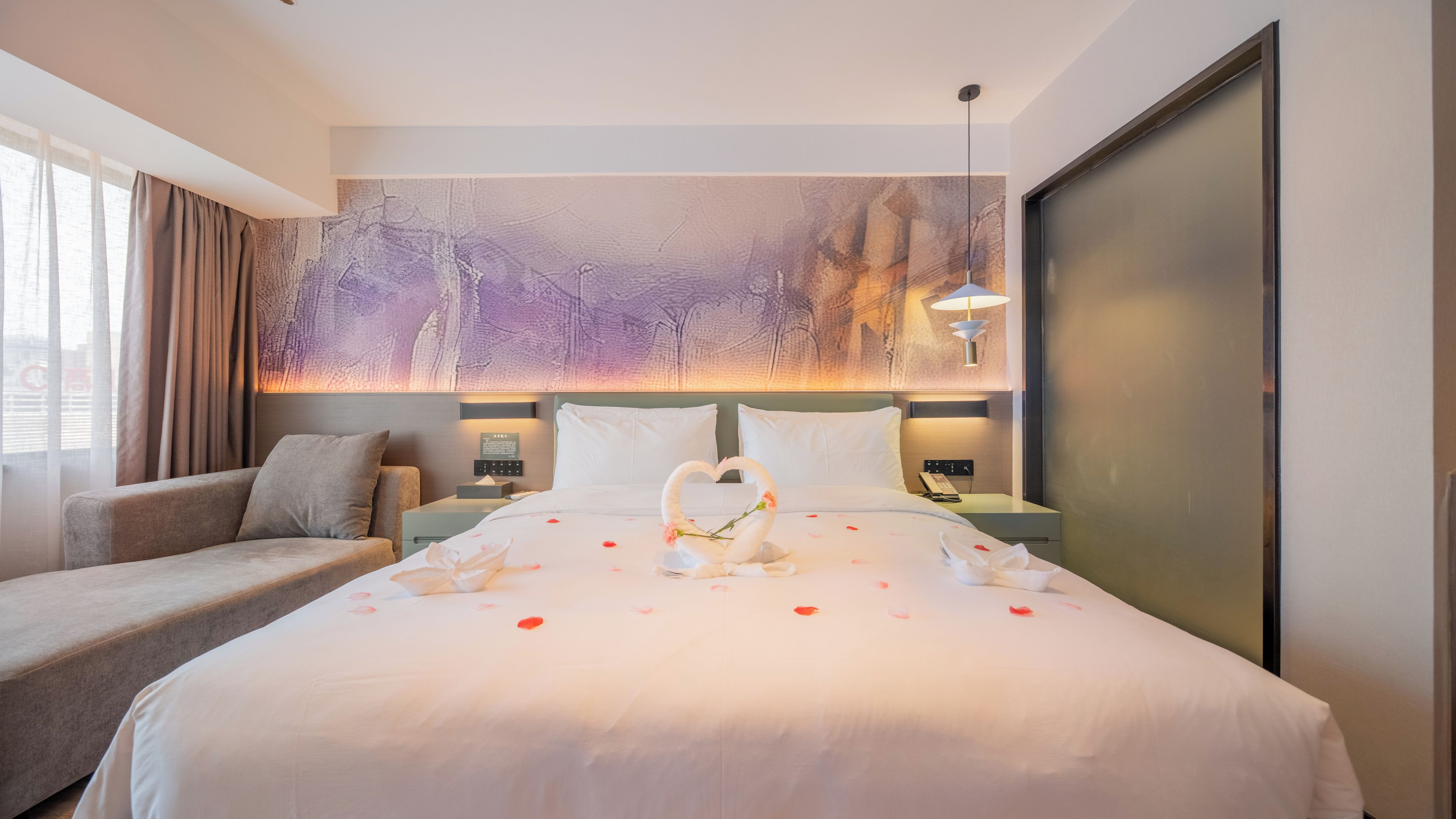 A hotel room with a large bed, a sofa, a nightstand, and a wall-mounted lamp.