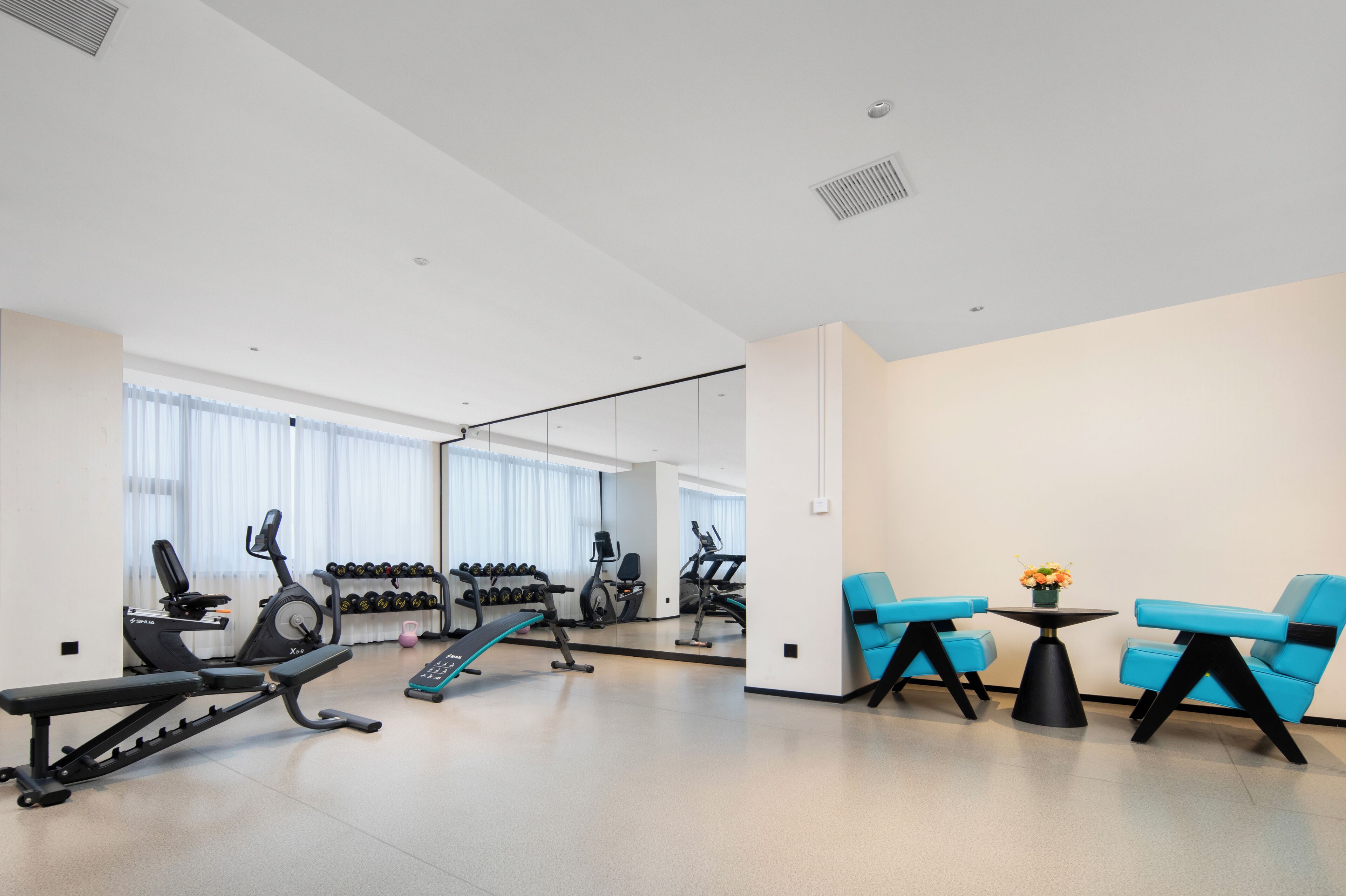A modern gym with exercise equipment, a mirror, and blue chairs.