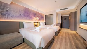 Ein Hotelzimmer mit zwei Betten, einem Sofa, einem an der Wand befestigten Fernseher und einem großen abstrakten Gemälde.