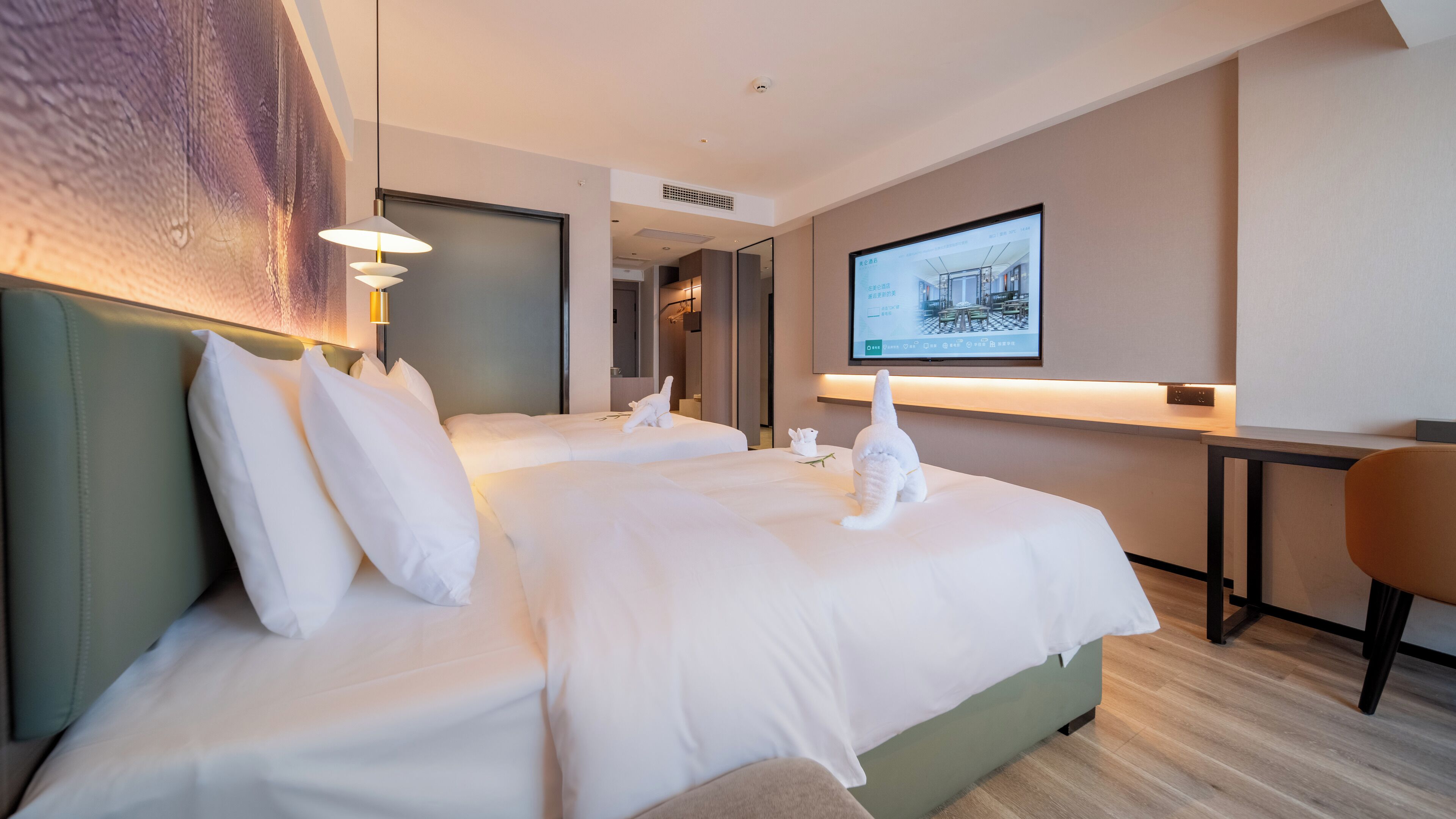 Ein modernes Hotelzimmer mit zwei Betten, einem Schreibtisch und einem an der Wand befestigten Fernseher.