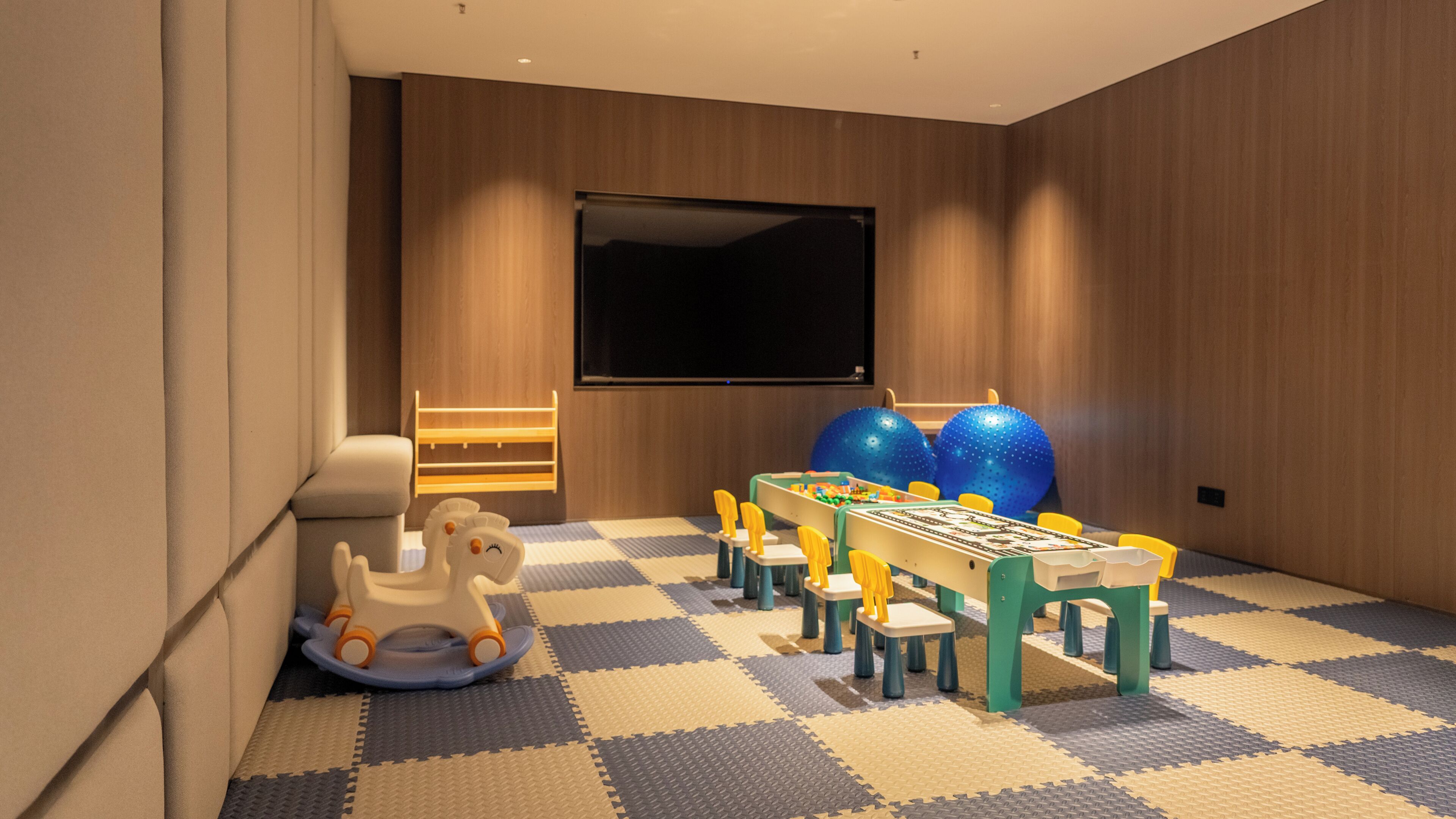 A children's play area with a table, chairs, a rocking horse, and exercise balls.