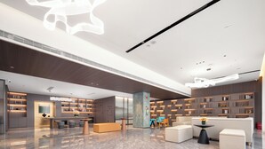 Eine großzügige Lobby mit modernem Design, inklusive einer zentralen Sitzecke, eines großen Bücherregals und einer auffälligen Deckenleuchte.