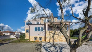 Una casa moderna de dos pisos con balcón, fachada de piedra y cielo azul despejado.