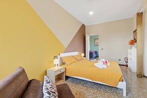 A hotel room with a bed, bedside table, lamp, and a small seating area with a couch and pillows. - La Caravella: Stresa Lake & Islands View Balcony, Stresa, Italy (Stresa)